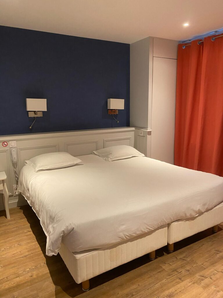 Chambre PMR : grand lit, mur bleu foncé et rideaux orange