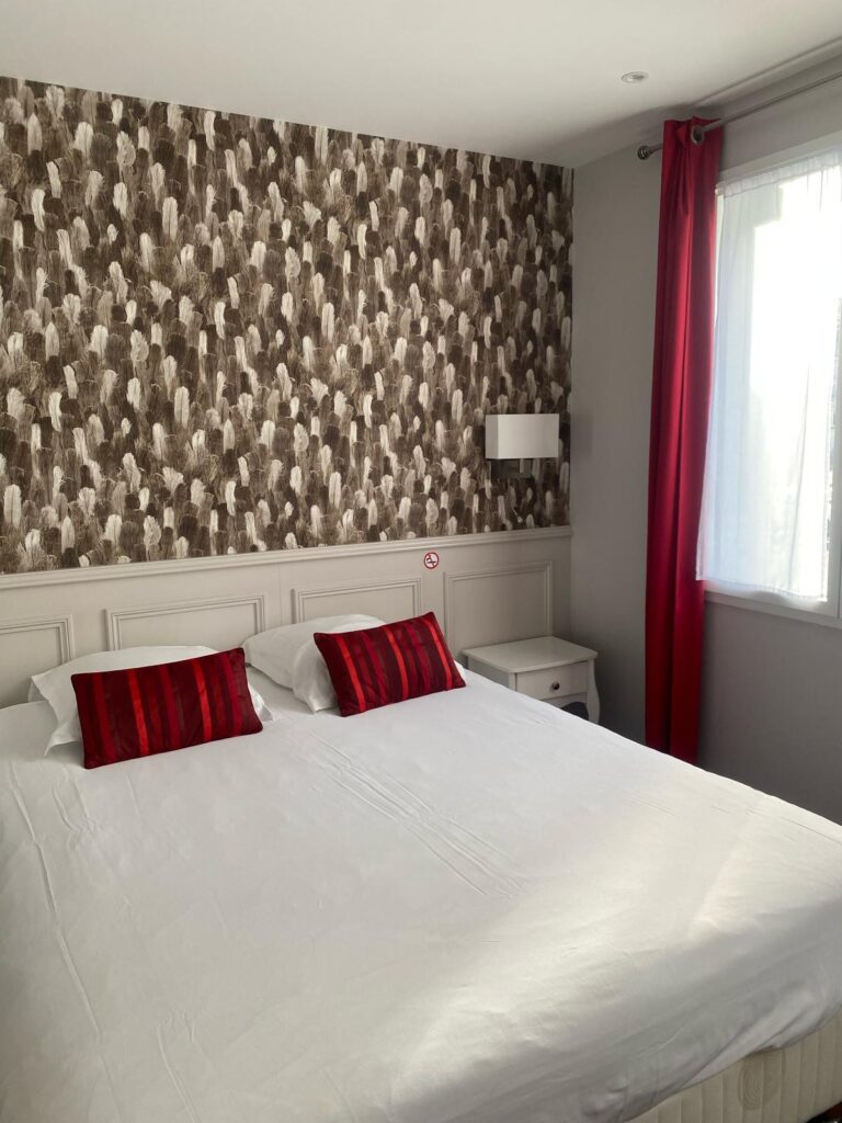 Chambre avec lit double, coussins rouges et papier peint graphique