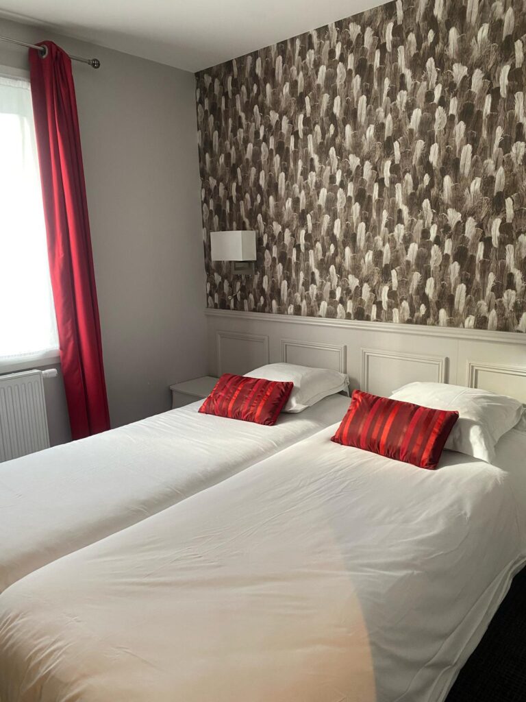 Chambre avec deux lits simples, coussins rouges et papier peint