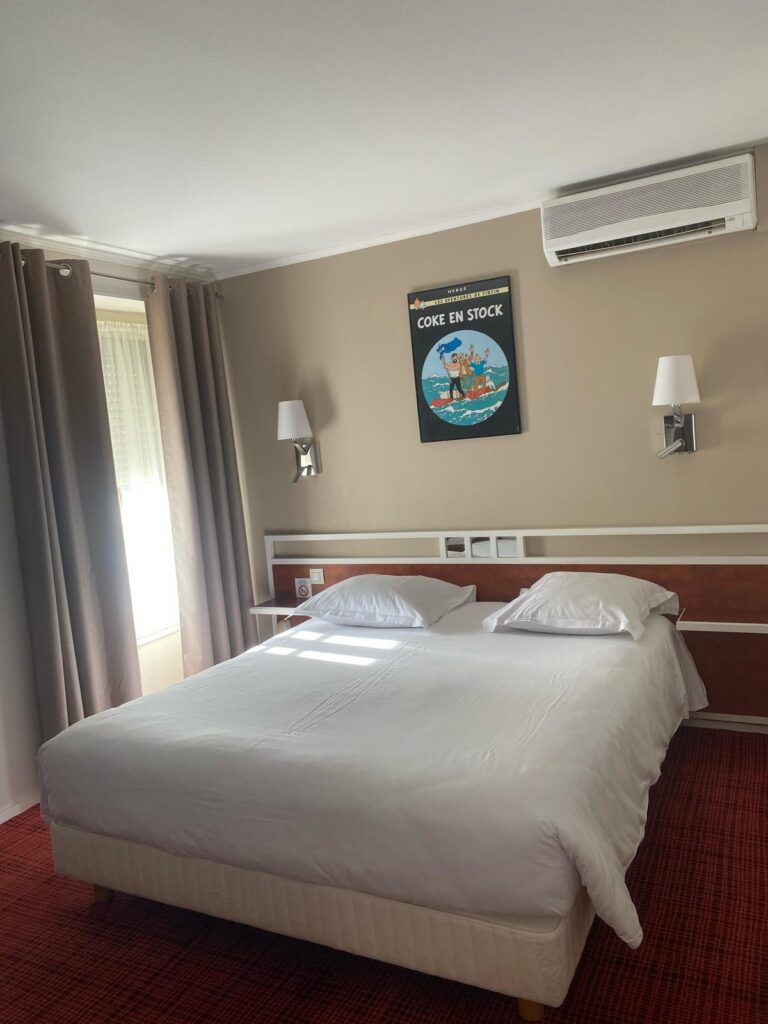 Chambre avec grand lit, affiche de BD et climatisation murale