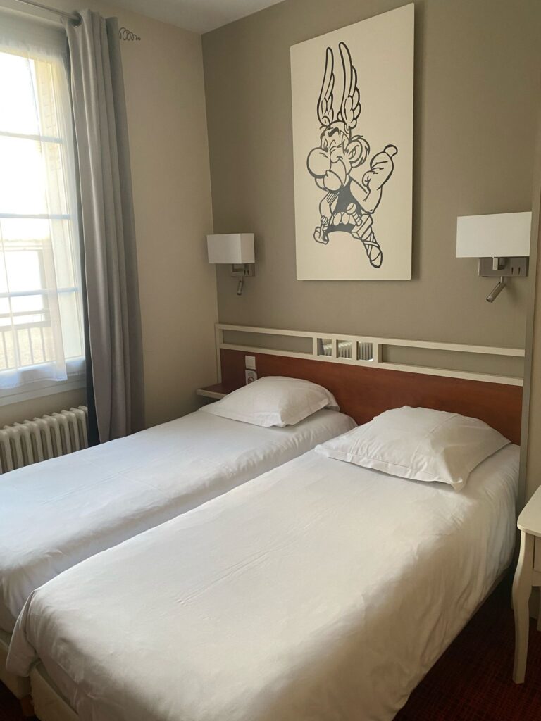 Chambre avec deux lits simples et affiche de BD au mur
